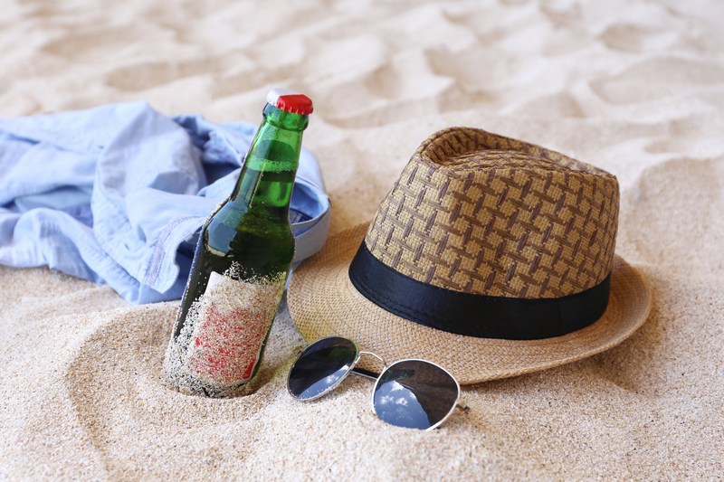 בקבוק בירה משקפי שמש וכובע על חול בים